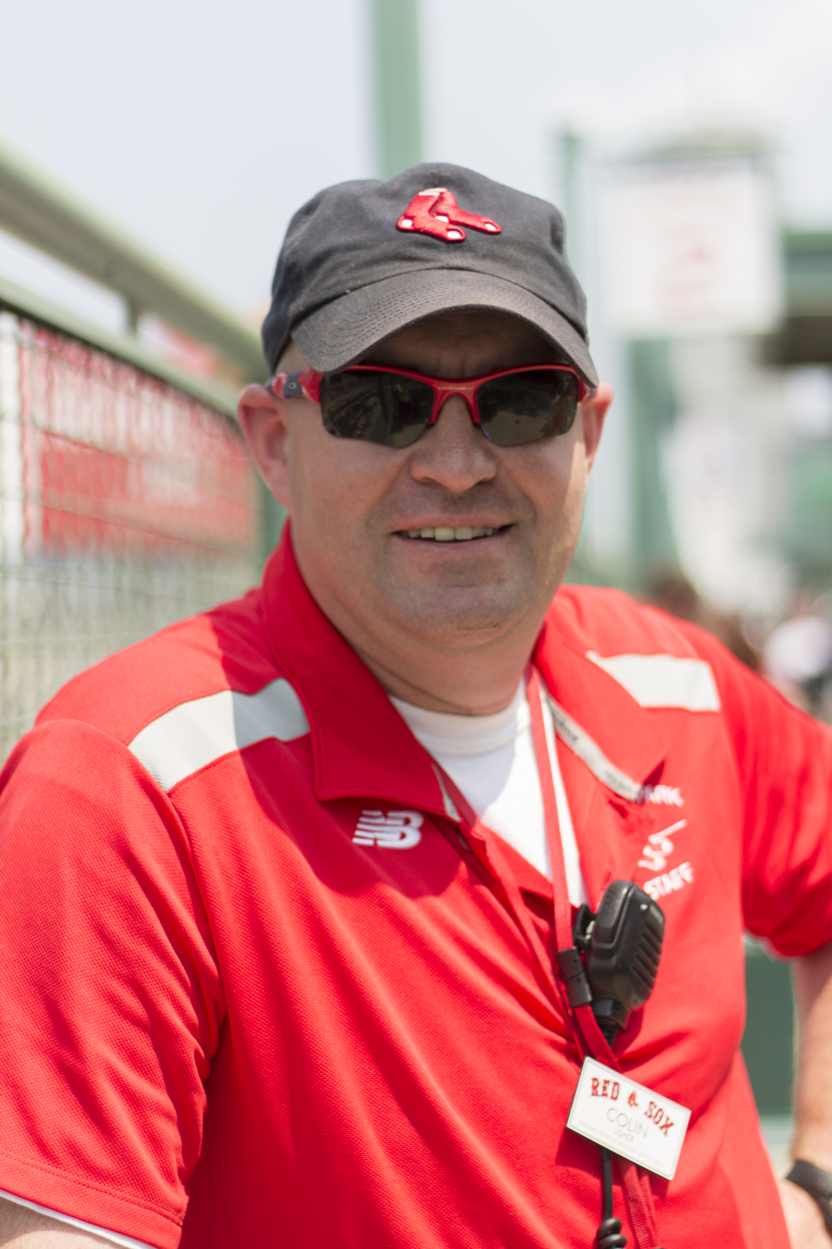 A white man wearing sunglasses and a Red Sox usher uniform smiles at the camera.