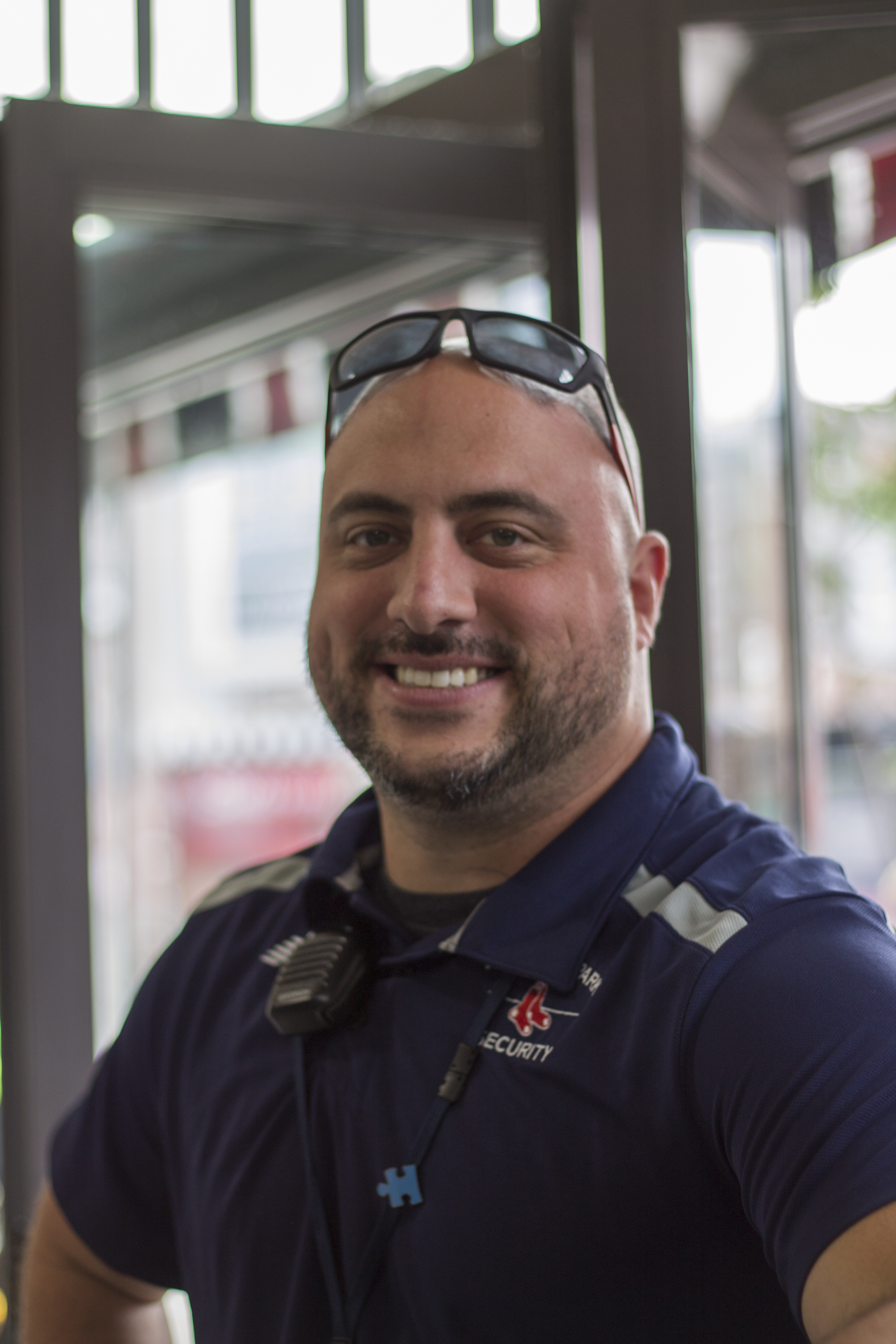 A white man wearing sunglasses on his head and a Red Sox security uniform smiles at the camera.
