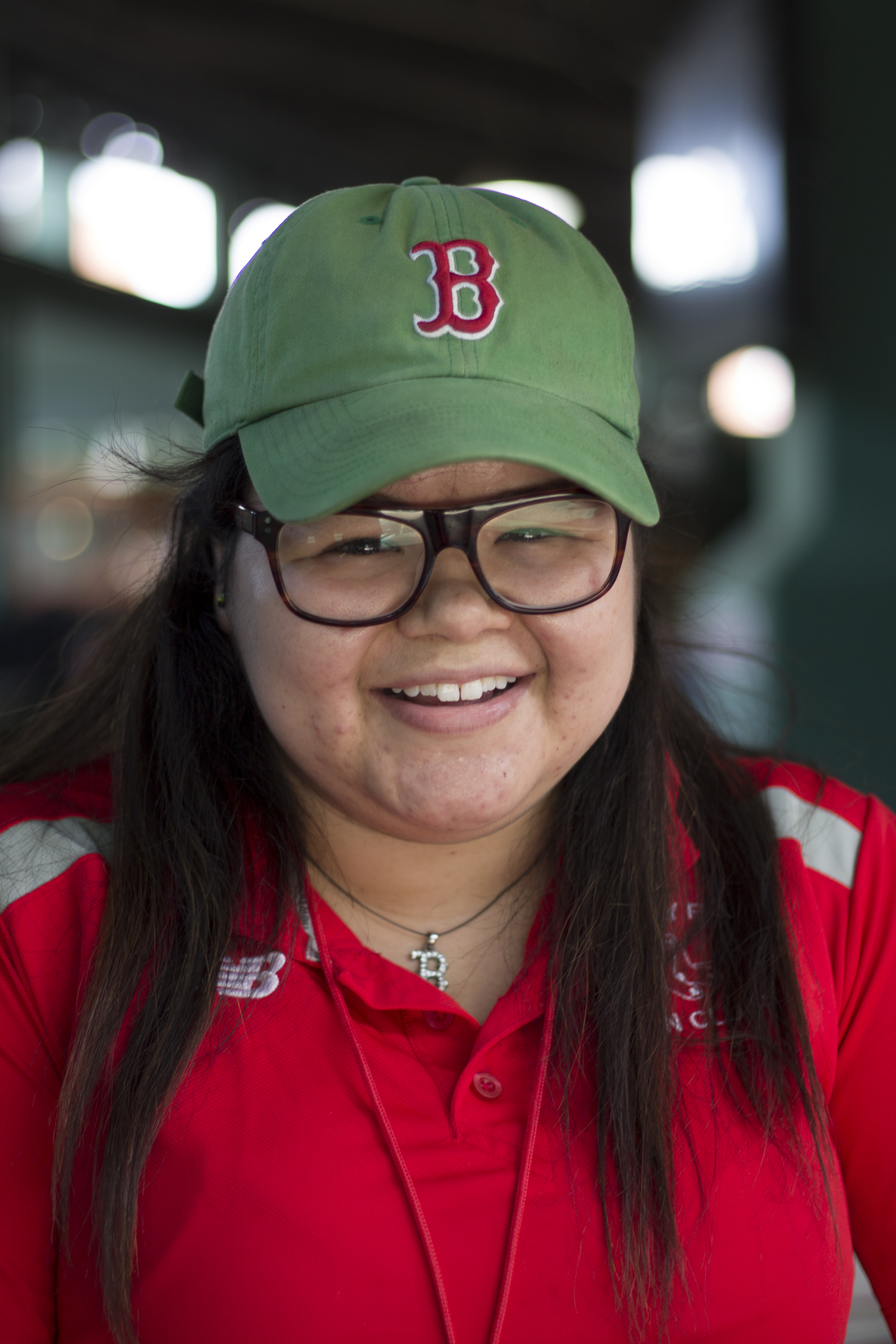A woman wearing a green Red Sox hat and square glasses smiles at the camera.